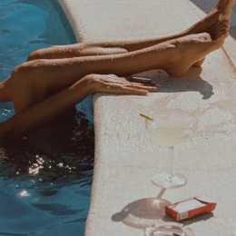 legs hanging out of a pool and a drink